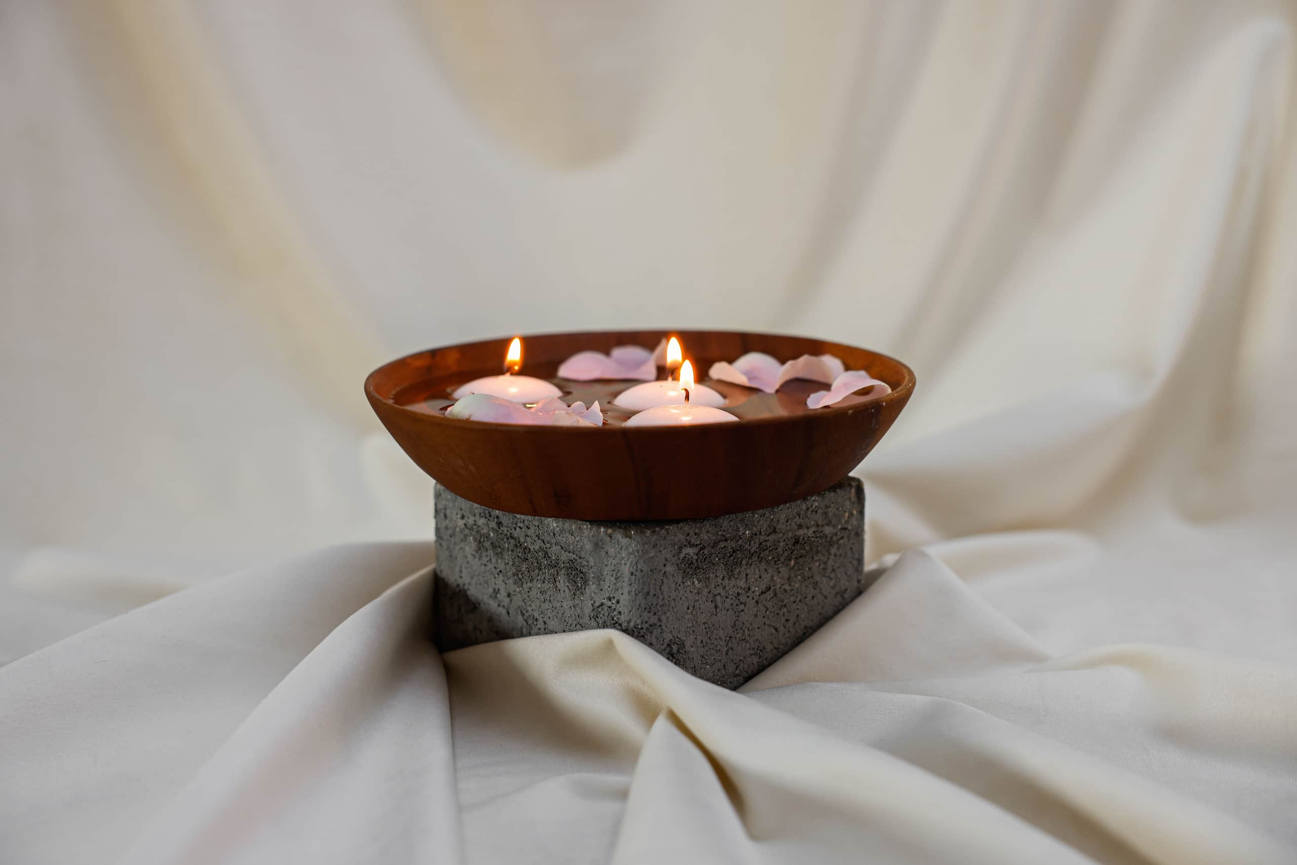 Wooden bowl with floating candles and petals on a stone base