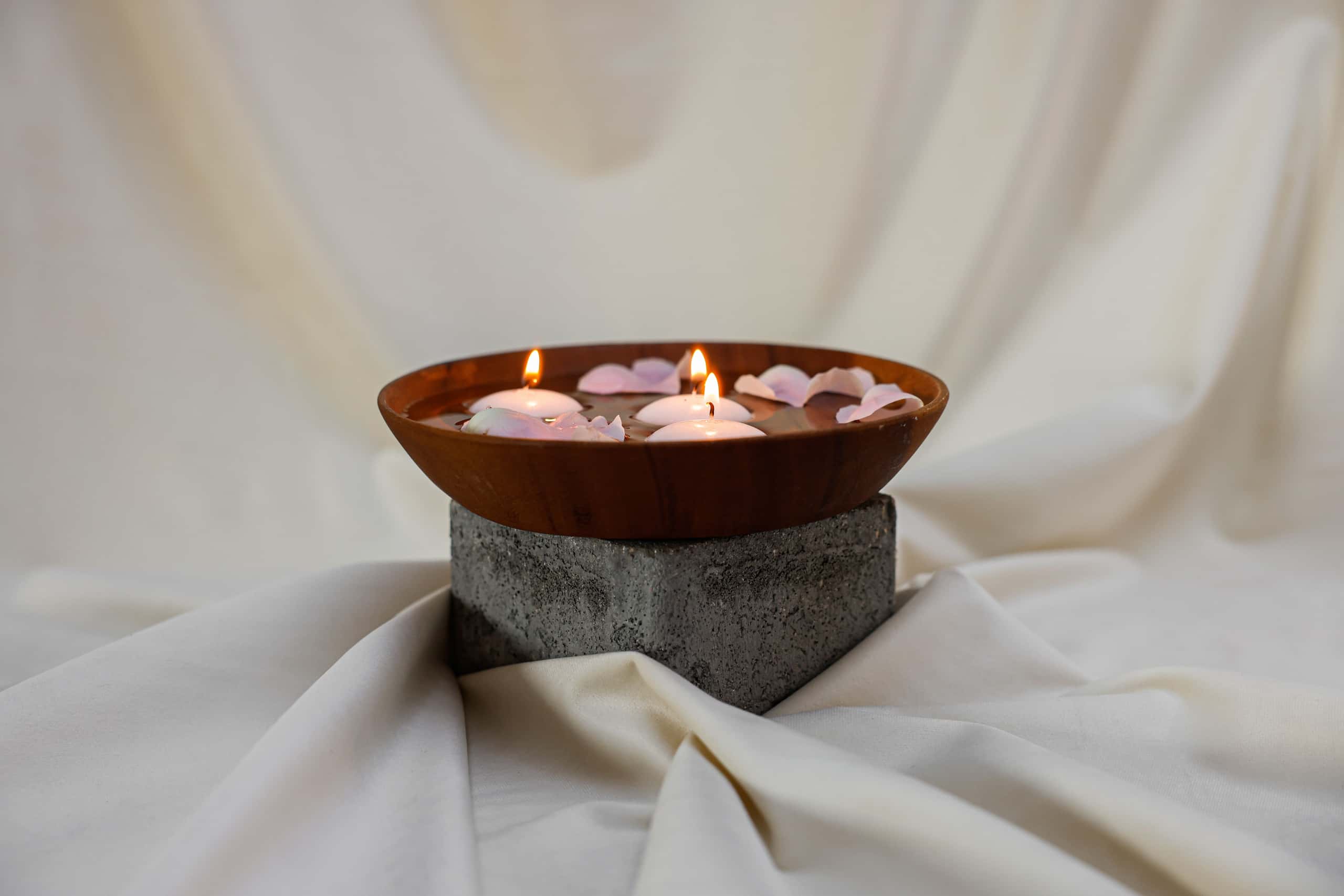 Wooden bowl with floating candles and petals on a stone base